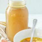 A bowl of chicken noodle soup next to a jar of broth.