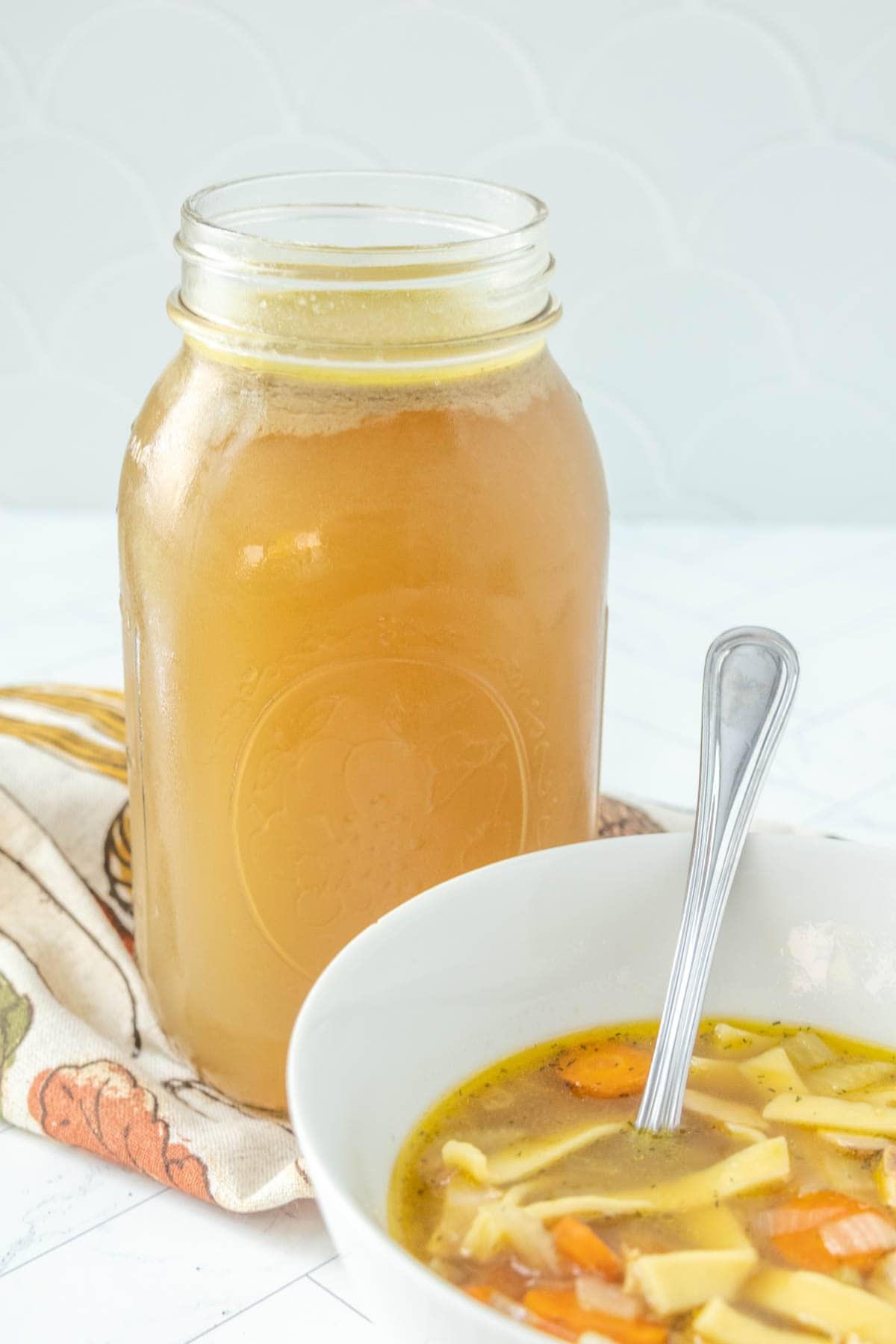 A bowl of chicken noodle soup next to a jar of broth.