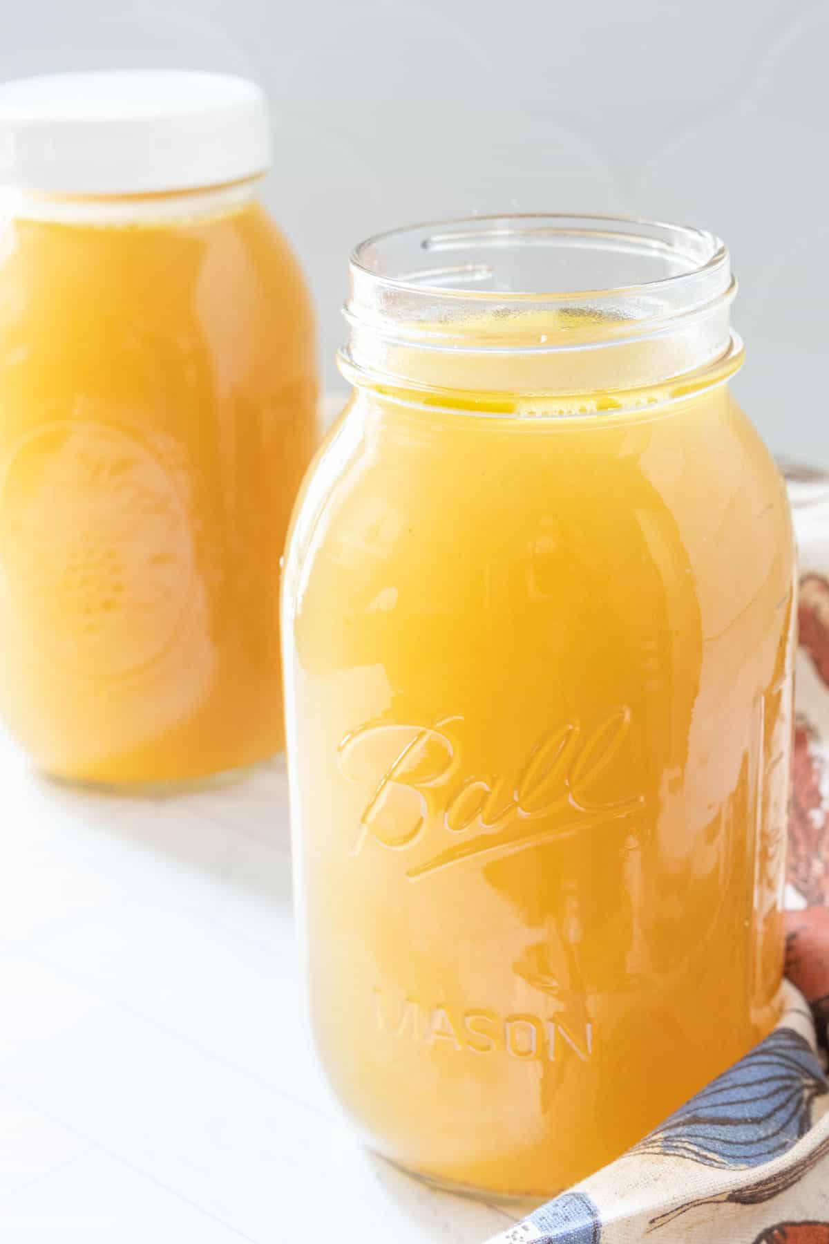 Two mason jars of chicken broth on a table.