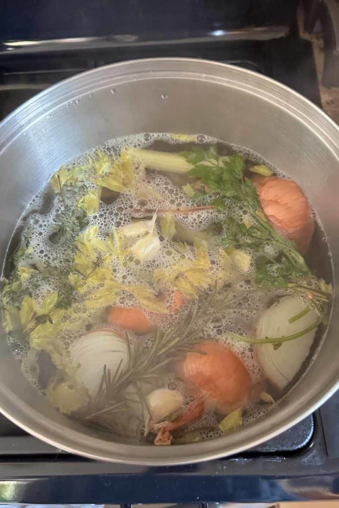 A pot filled with vegetables and herbs on the stove.
