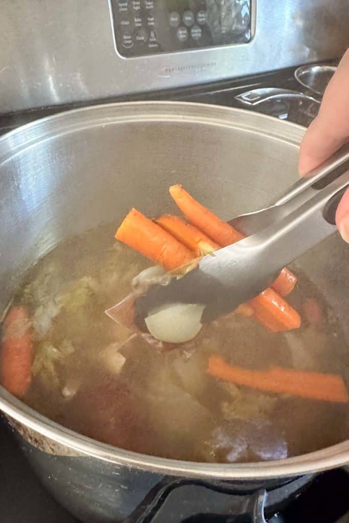 A person using a spoon to stir vegetables in a pot.