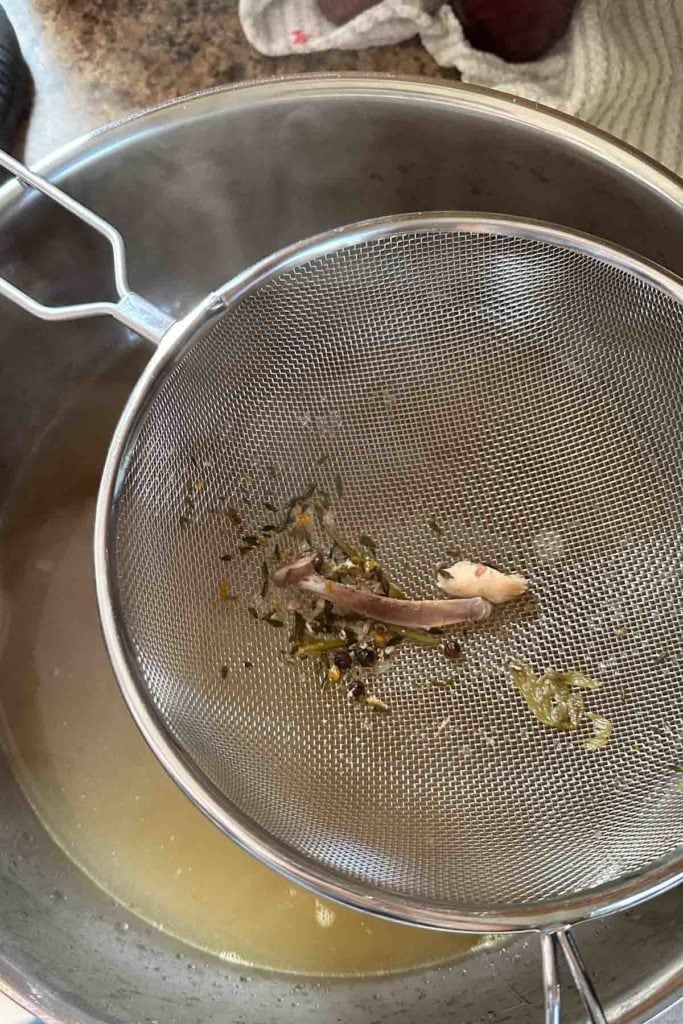 A metal strainer filled with liquid and herbs.