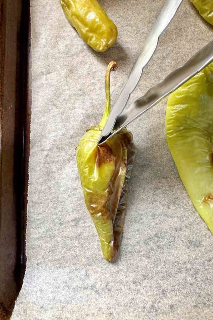 A pair of tongs turning a pepper on a baking sheet.