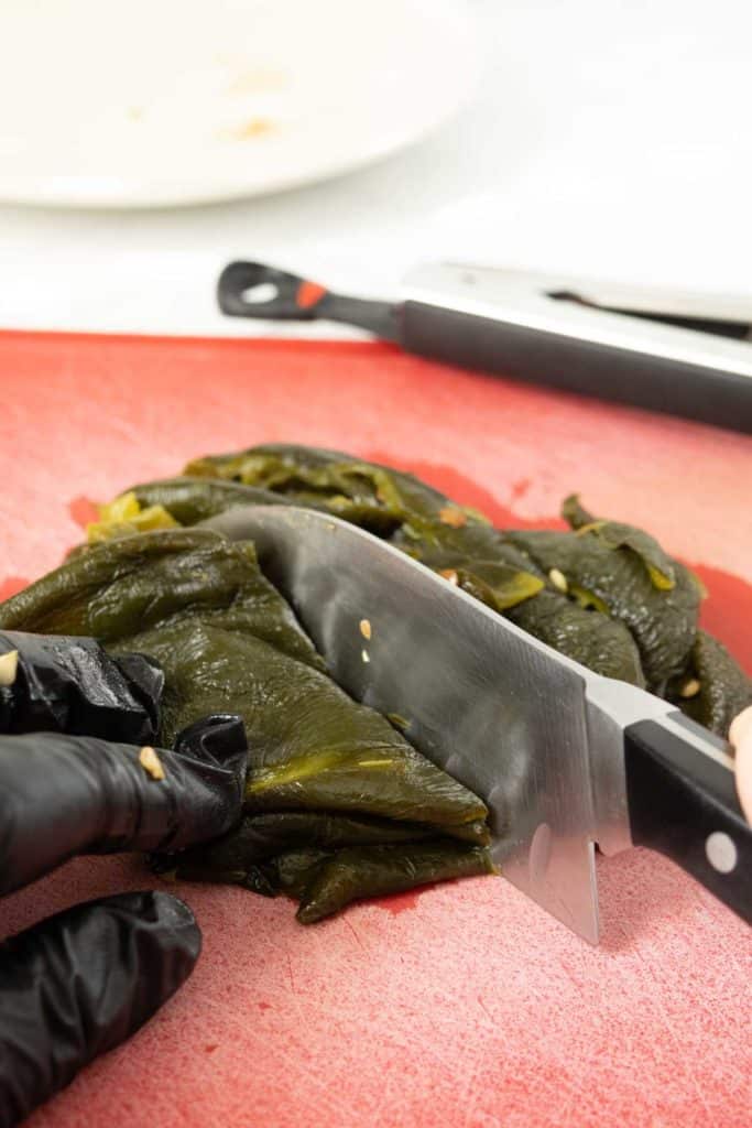 A person in black gloves is cutting green peppers on a cutting board.