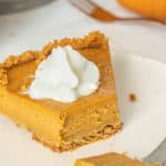 A slice of pumpkin pie on a plate with whipped cream.