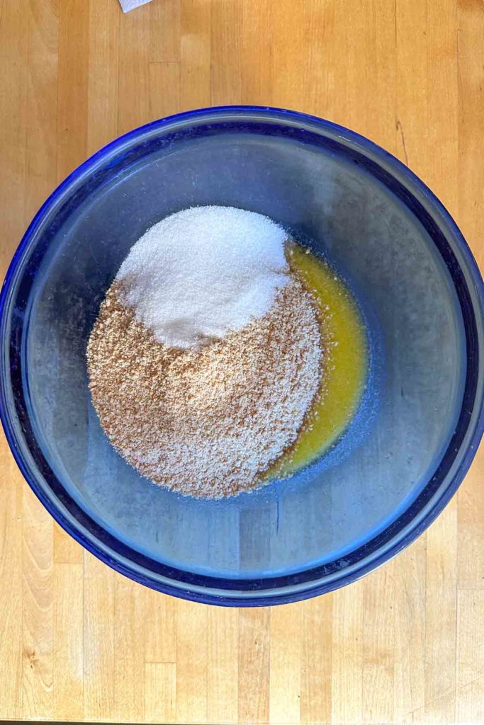 A blue bowl filled with a mixture of graham cracker crumbs and sugar.