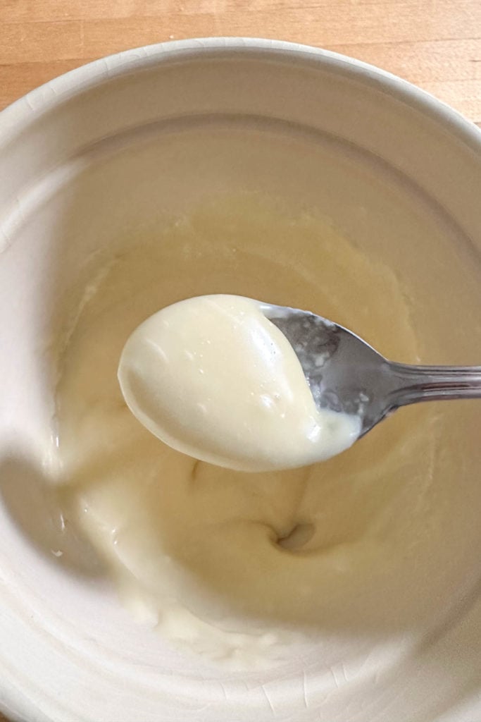 A spoonful of white chocolate ganache in a bowl on a wooden table.