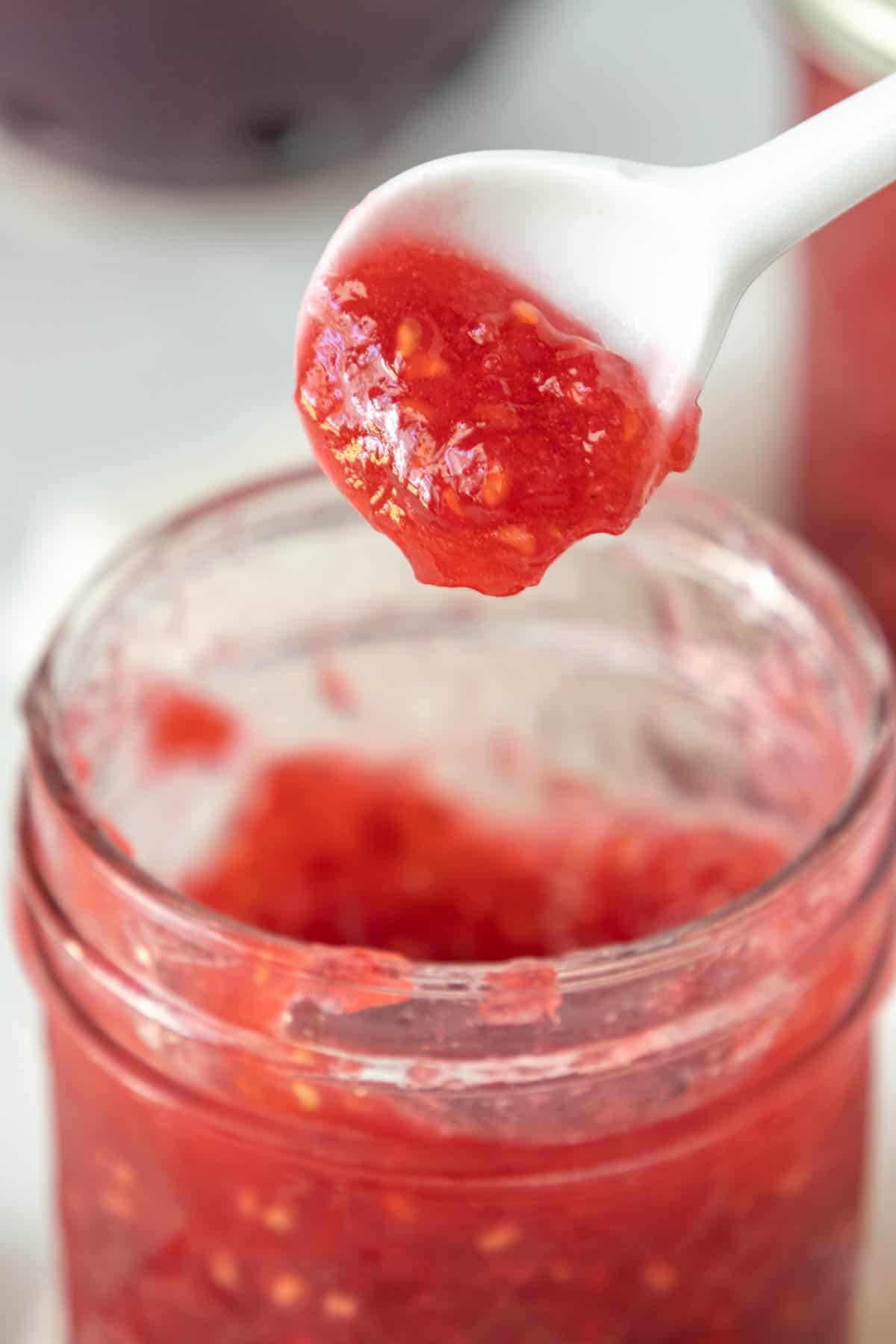 Raspberry jam in a jar with a spoon.