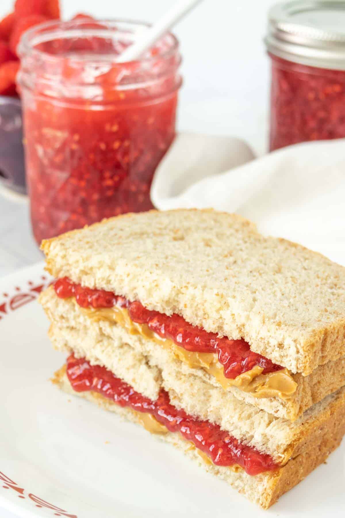 Raspberry jam sandwich on a plate with a jar of raspberry jam.