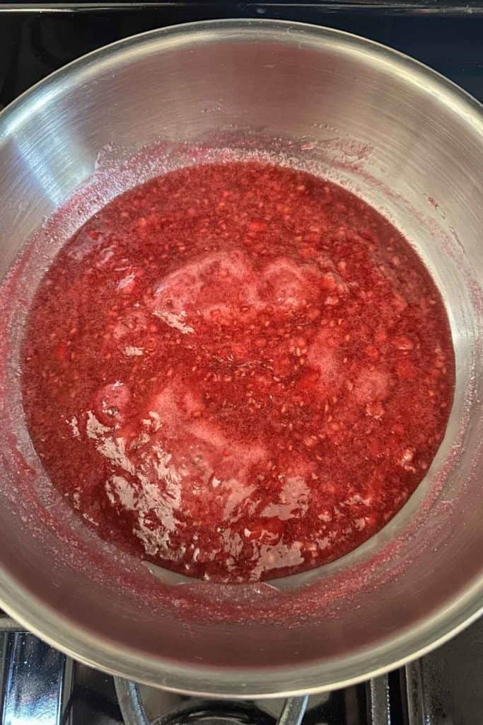 A pan full of raspberry jam cooking on a stove top.