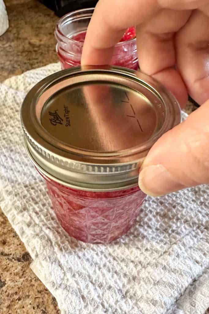 A person putting a lid on a jar of jam.
