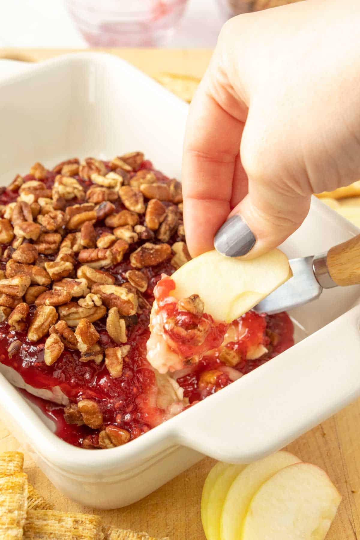 A person is dipping into a dish of baked brie.