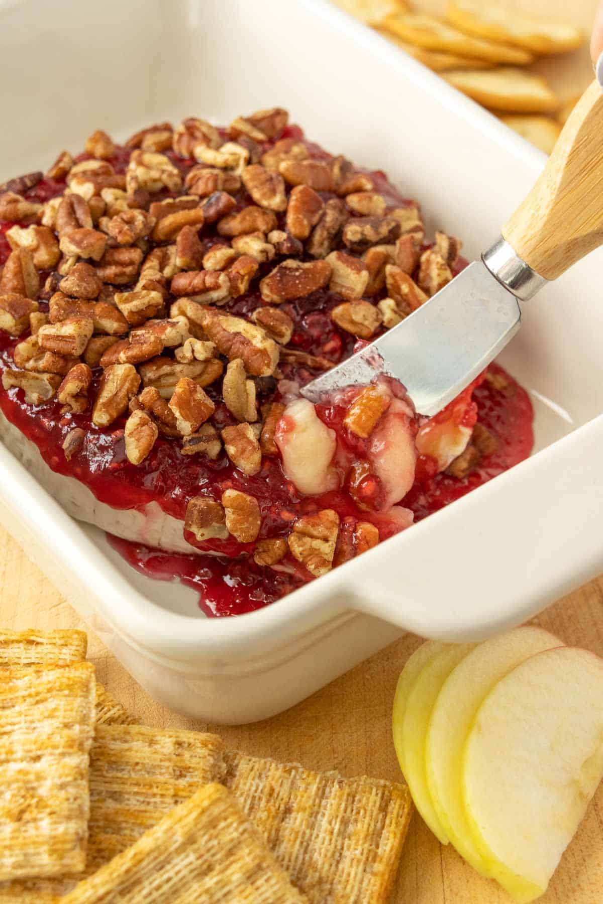 A person is slicing a dish of baked brie.