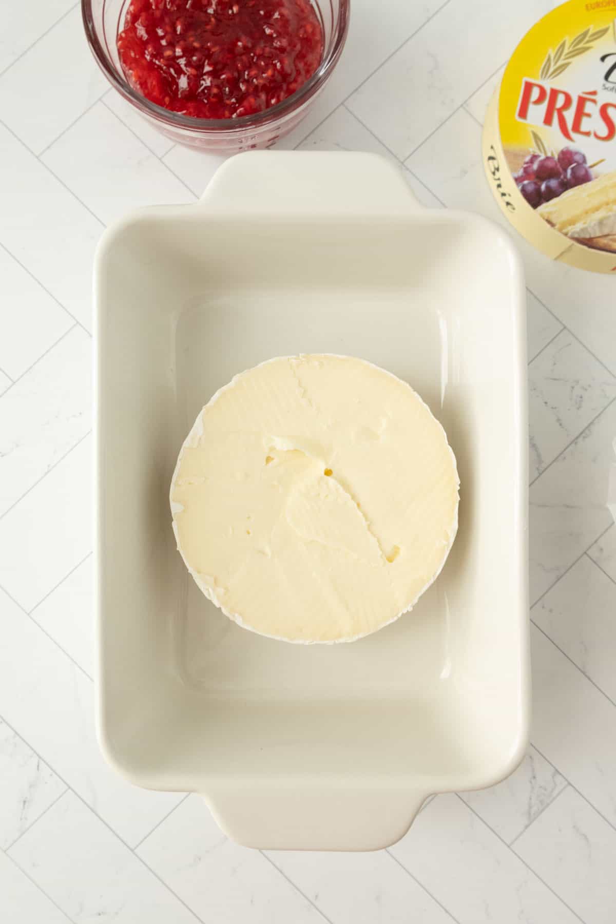 A wheel of brie on a white plate next to a bowl of jam.