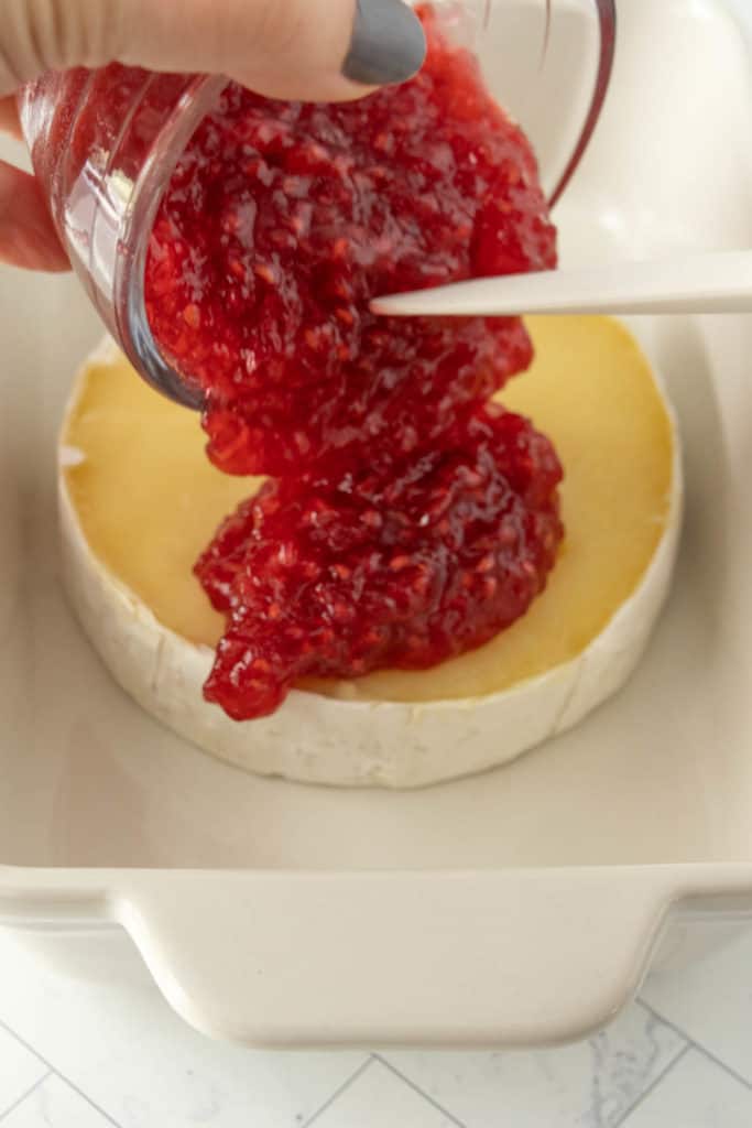 A person is dipping a spoon into a bowl of raspberry jam.