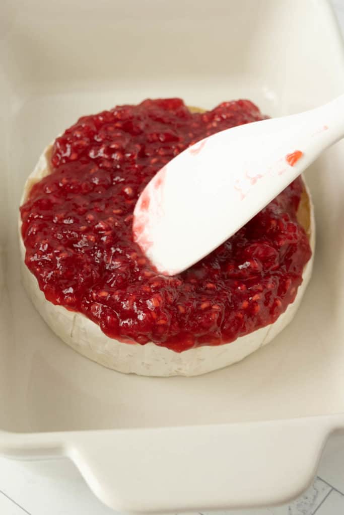 A spoon is being used to spread jam on a brie.