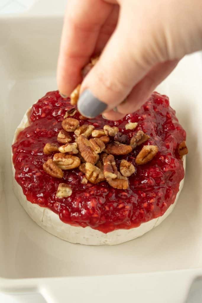 A person putting a pecan on a piece of cheese.