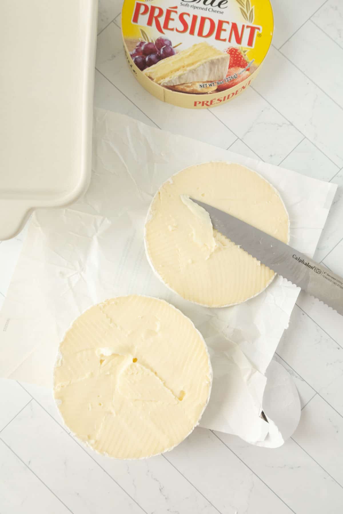 A wheel of brie with the top cut off on top of a piece of paper.