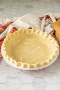 A pie crust on a table next to a rolling pin.