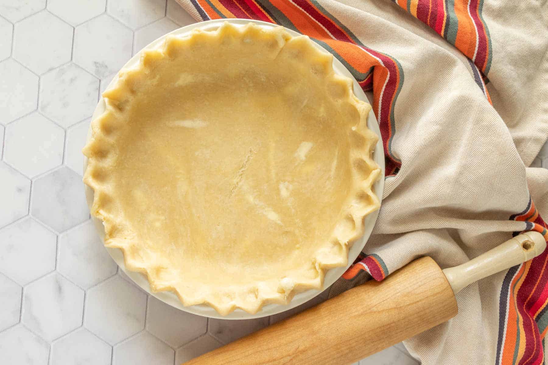 A pie crust on a table next to a rolling pin.