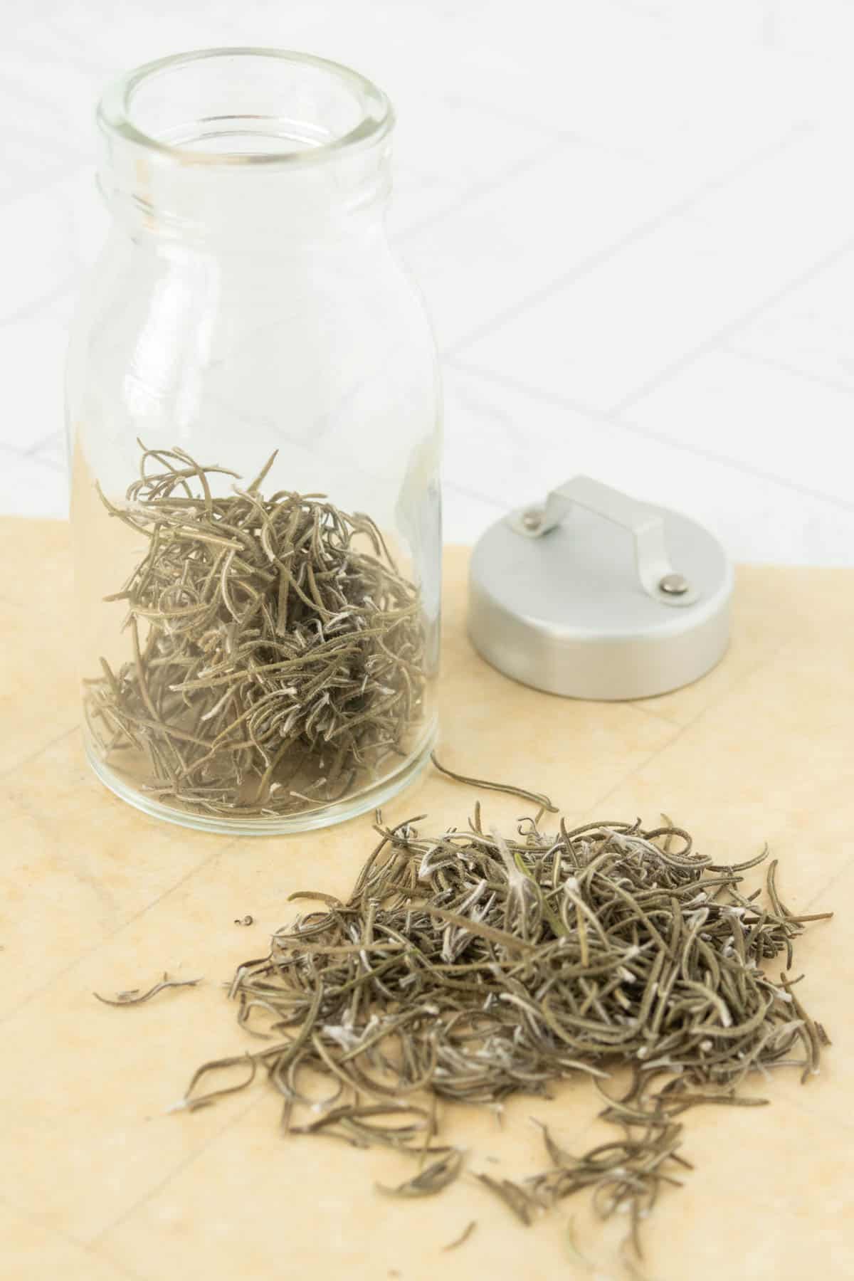 A glass jar filled with dried rosemary leaves.