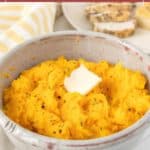 A bowl of creamy mashed butternut squash topped with a pat of butter, served alongside bread and a striped towel in the background.