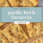 Sliced no-knead focaccia on a wooden cutting board, topped with minced garlic, herbs, and coarse salt. Text overlay reads "No Knead Garlic Herb Focaccia.