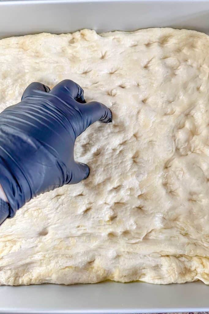 A person dimpling focaccia dough in a pan.