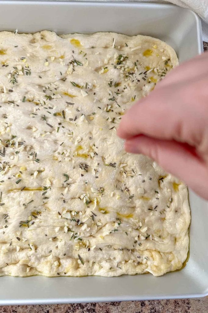 A person adding toppings to bread dough.