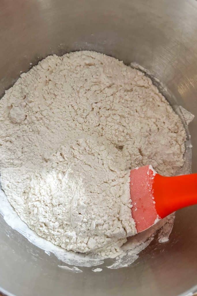 A bowl of flour with an orange spatula in it.