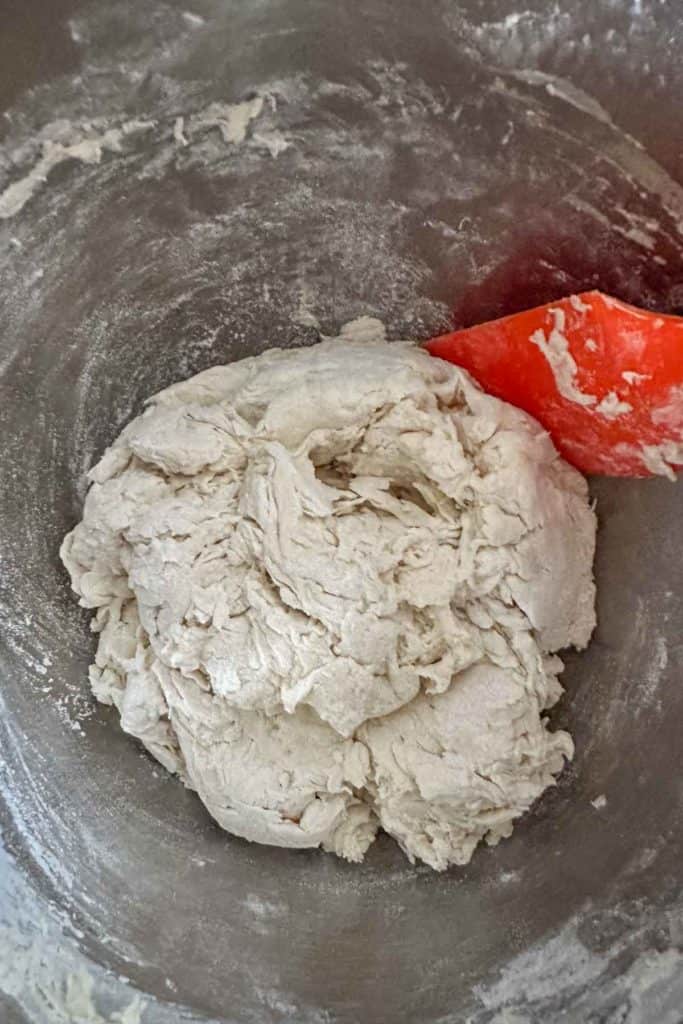 Dough being mixed in a bowl with an orange spatula.