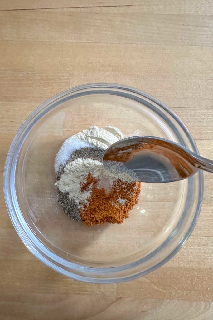 A spoonful of spices in a bowl on a wooden table.