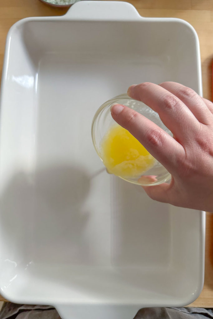 A person pouring melted butter into a baking dish.