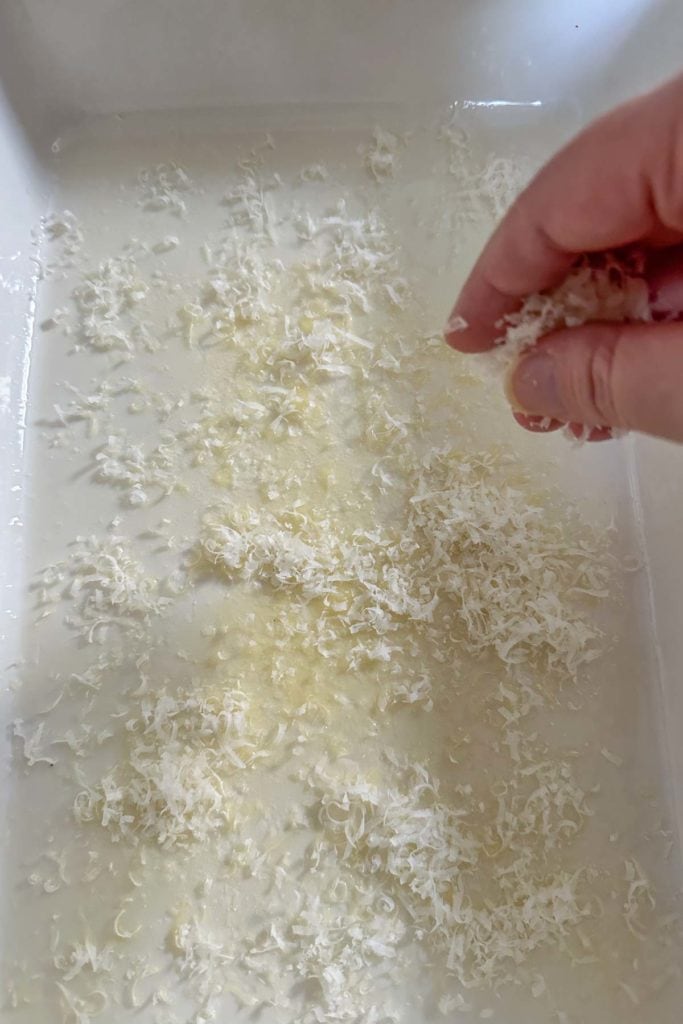 A person putting shredded cheese into a white dish.