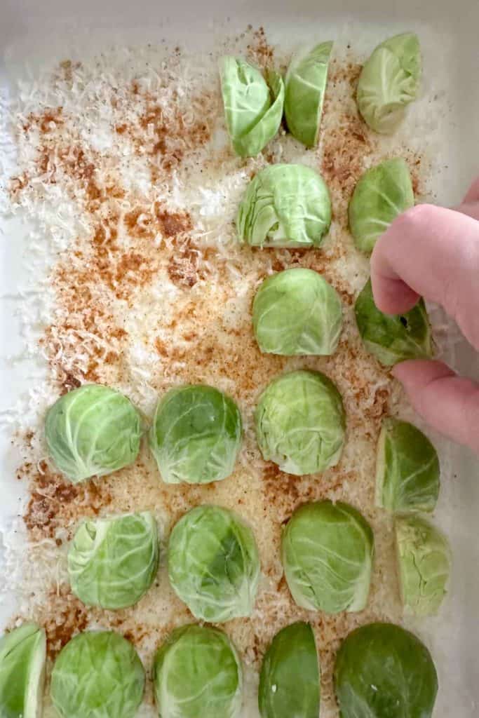 Brussels sprouts on a baking sheet with a hand placing them.