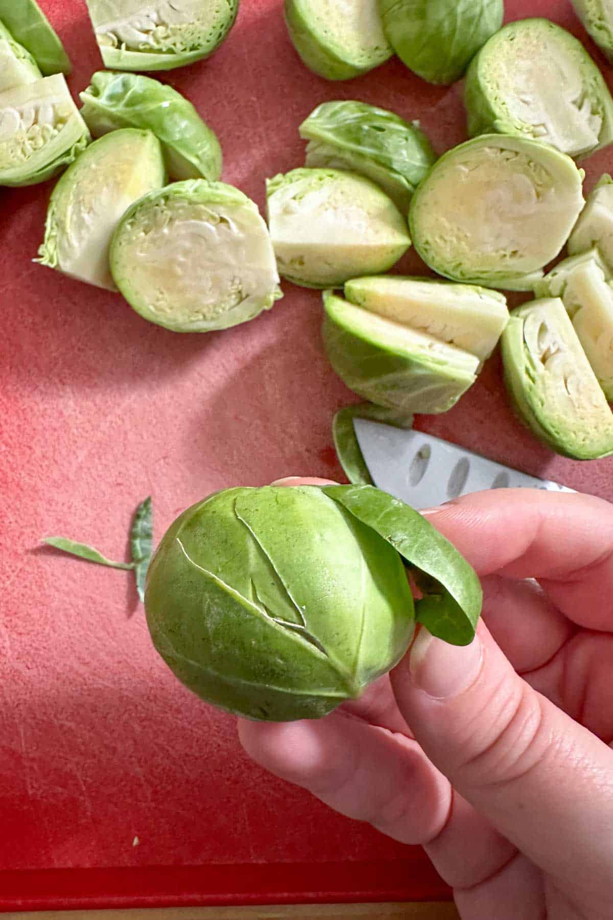 A person cutting brussel sprouts on a red cutting board.