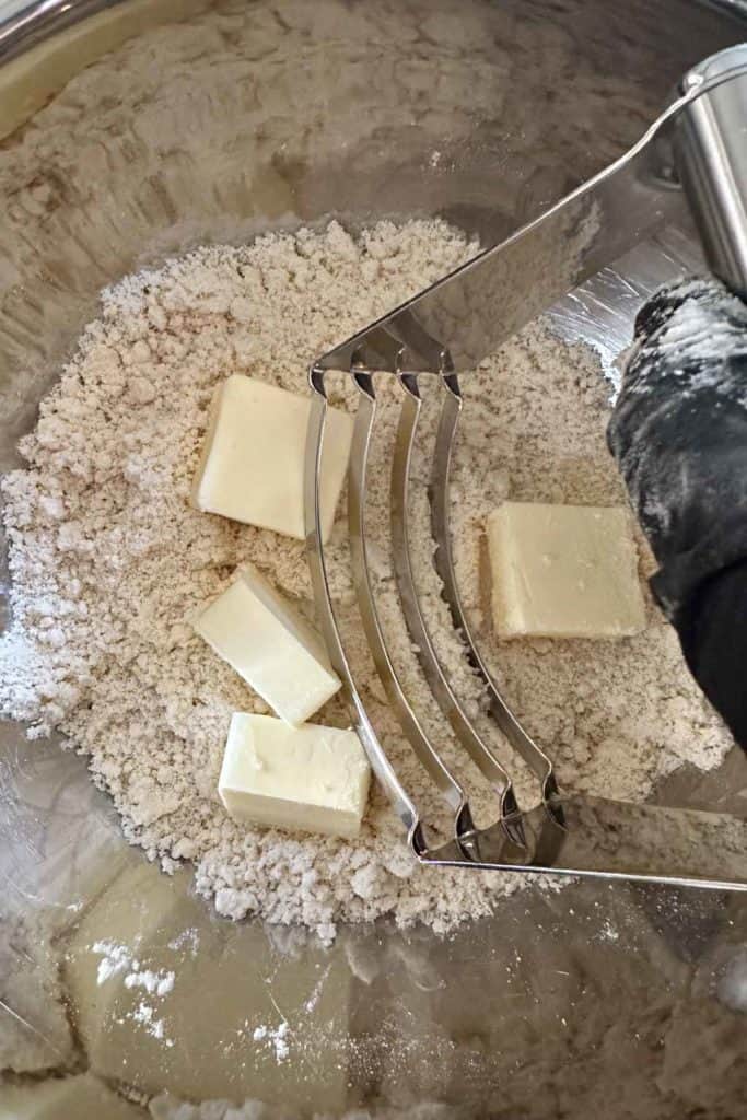 A person mixing butter and flour in a mixing bowl.