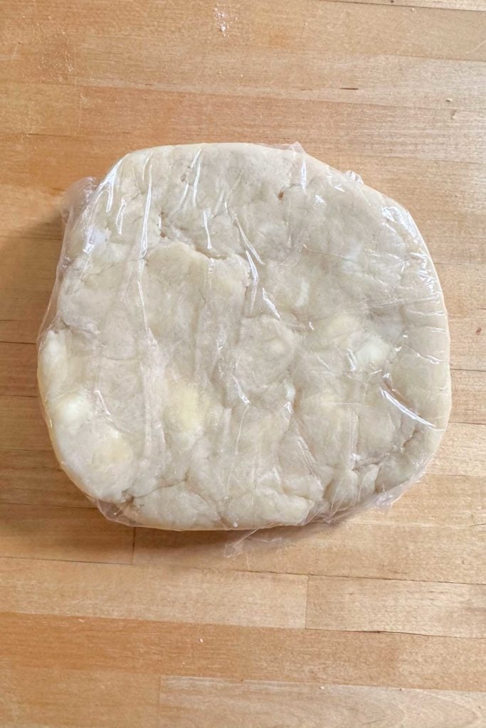 A piece of dough wrapped in plastic on a wooden table.