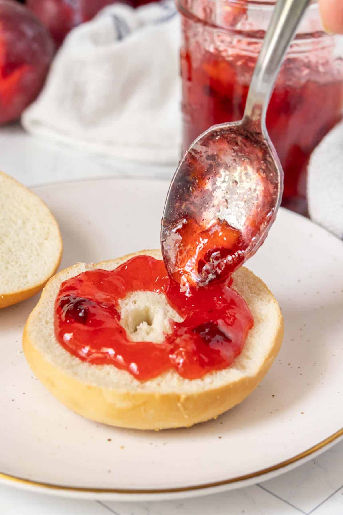 Plum jam on a bagel with a spoon.