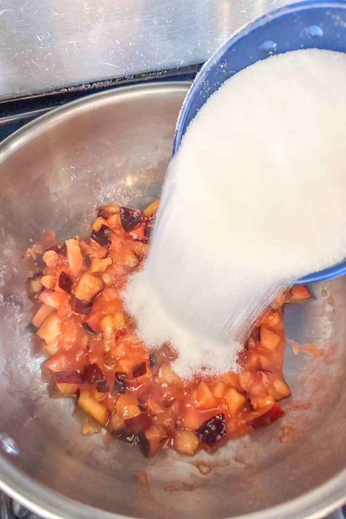 Sugar being poured into a bowl of fruit.