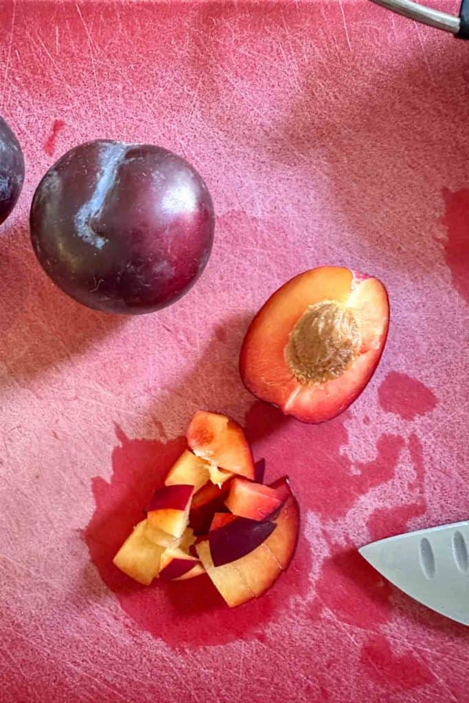 Sliced plums and a knife on a cutting board.