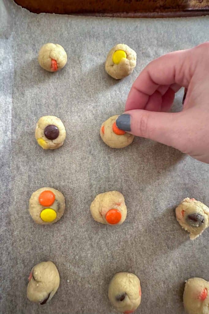 A person is putting candy on cookies on a baking sheet.