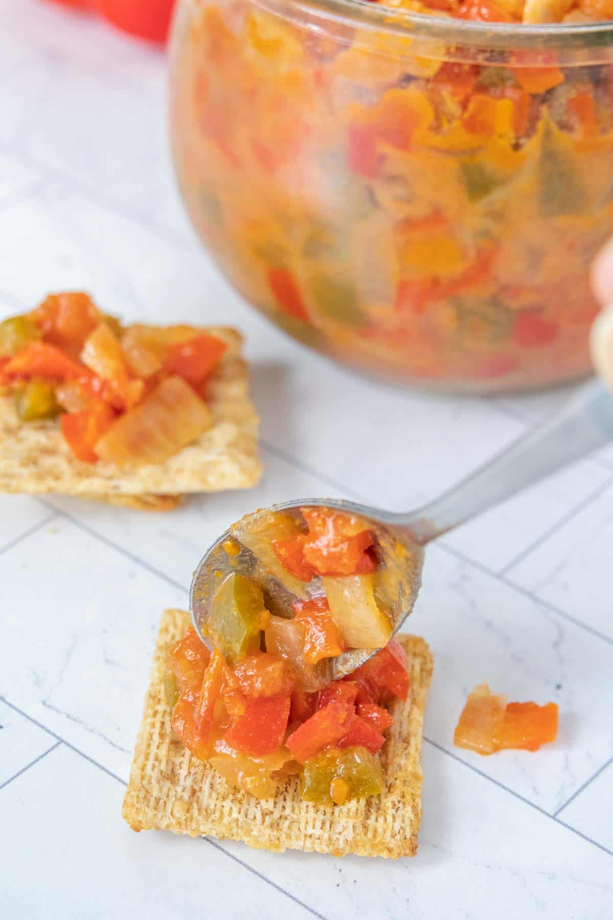 A person is holding a spoonful of salsa on a cracker.