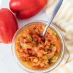 A bowl of red peppers next to a spoon.