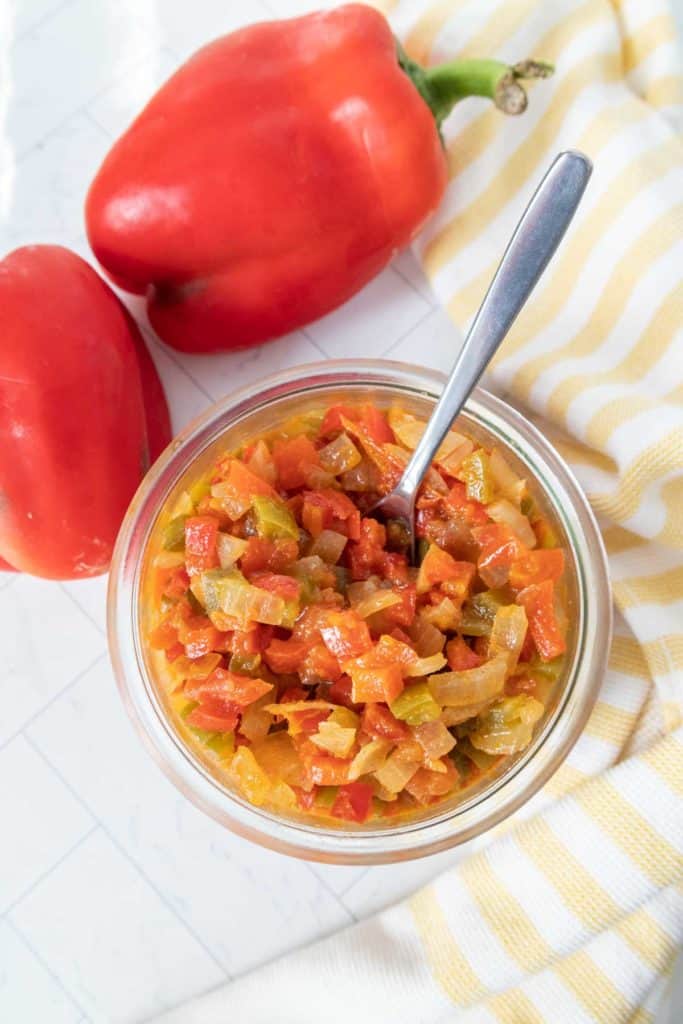 A bowl of red peppers next to a spoon.