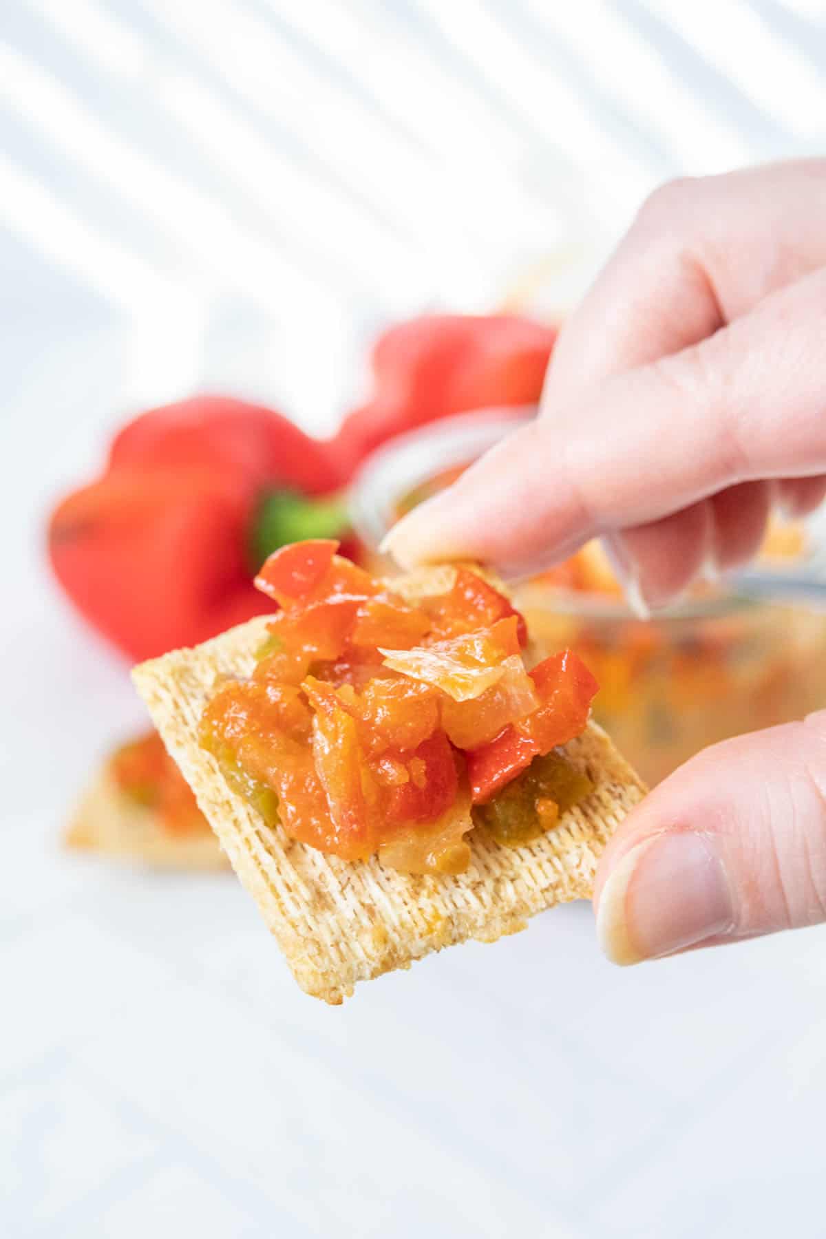 A hand is holding a cracker with pepper sauce on it.