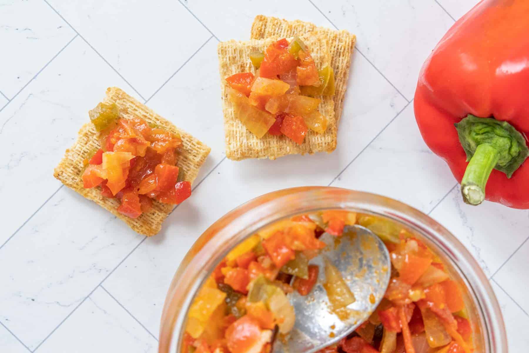 A jar of pepper relish with crackers and a spoon.