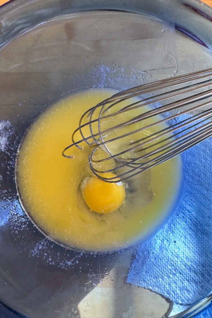 An egg being whisked in a glass bowl.