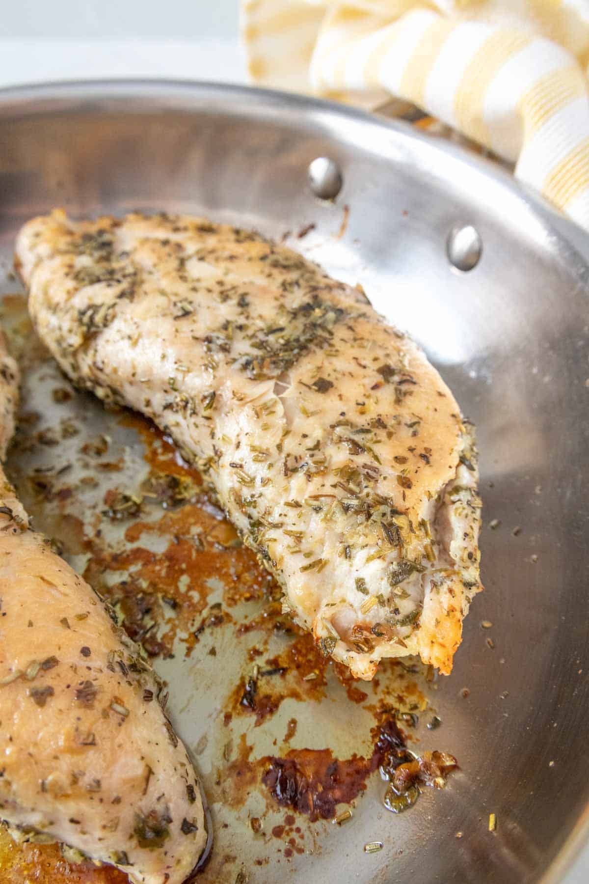 Two turkey tenderloins in a pan with herbs.