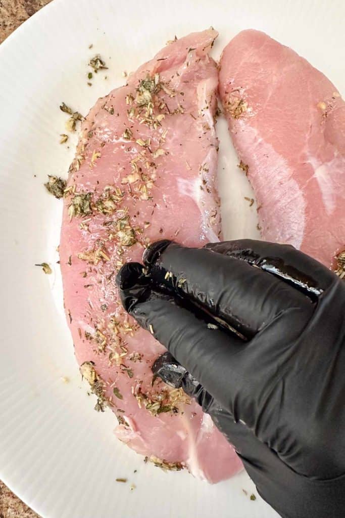 A person is rubbing herbs onto a piece of meat on a plate.